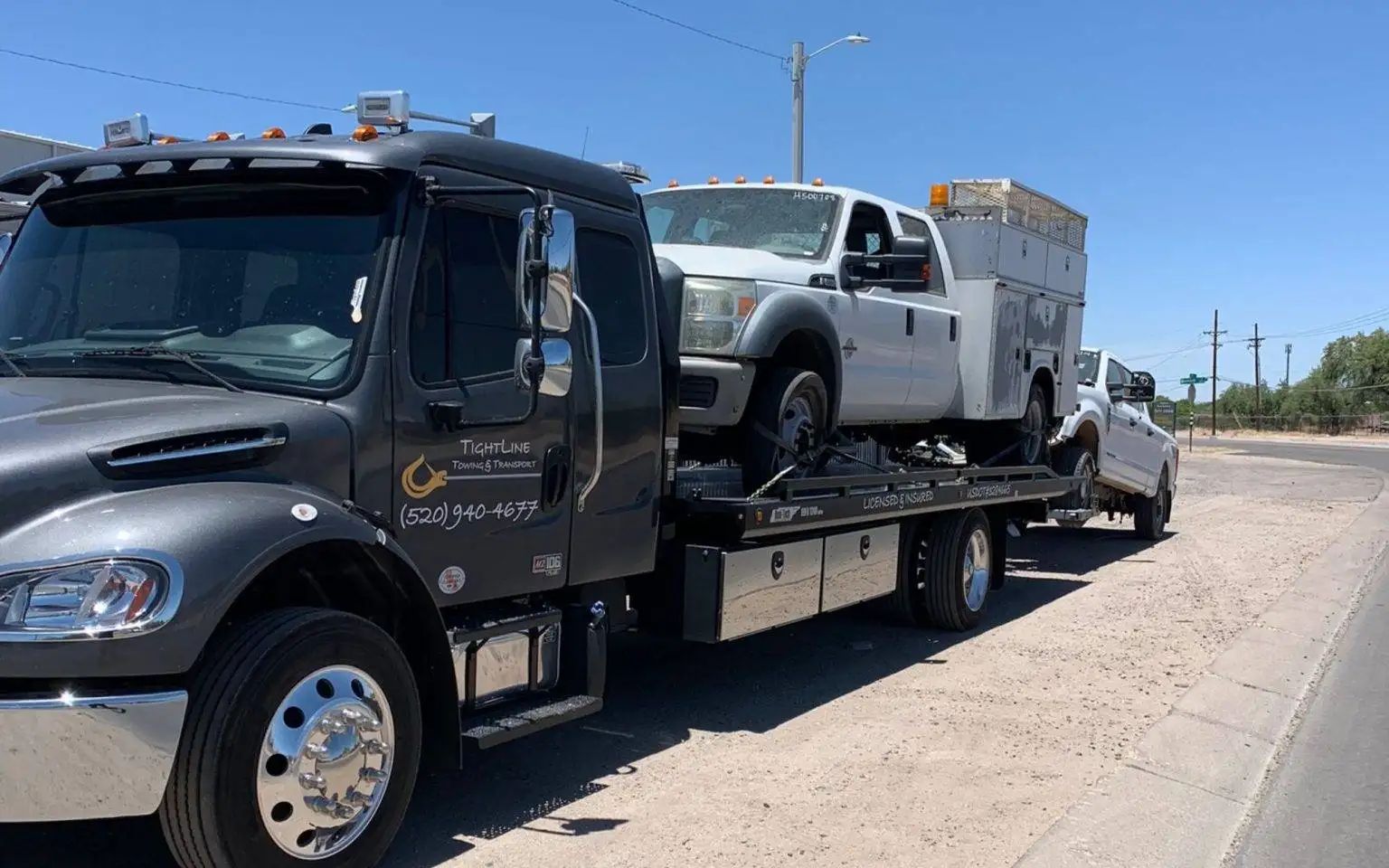 Tow truck hauling a white truck with a utility bed on a sunny day.