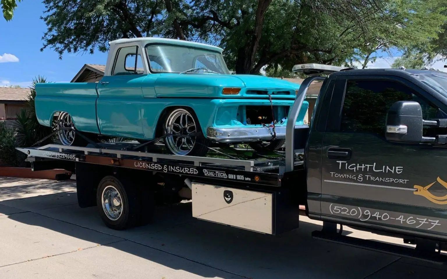 Teal classic pickup truck being transported on a flatbed tow truck.