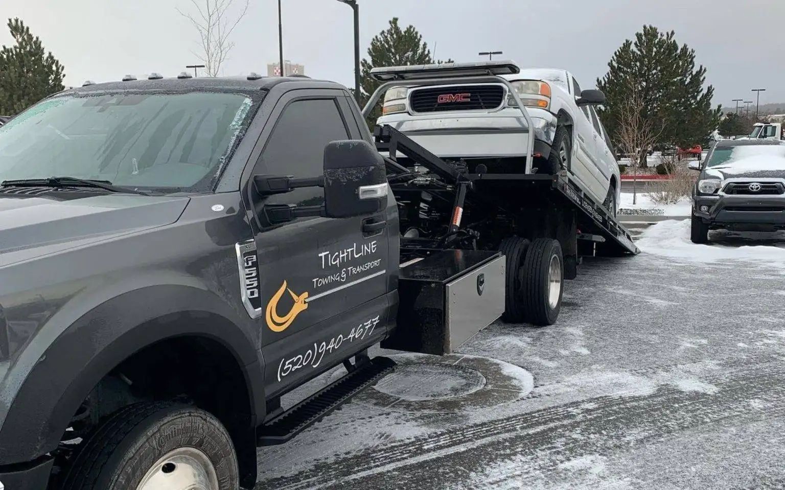 A tow truck loading a silver car on a snowy day.