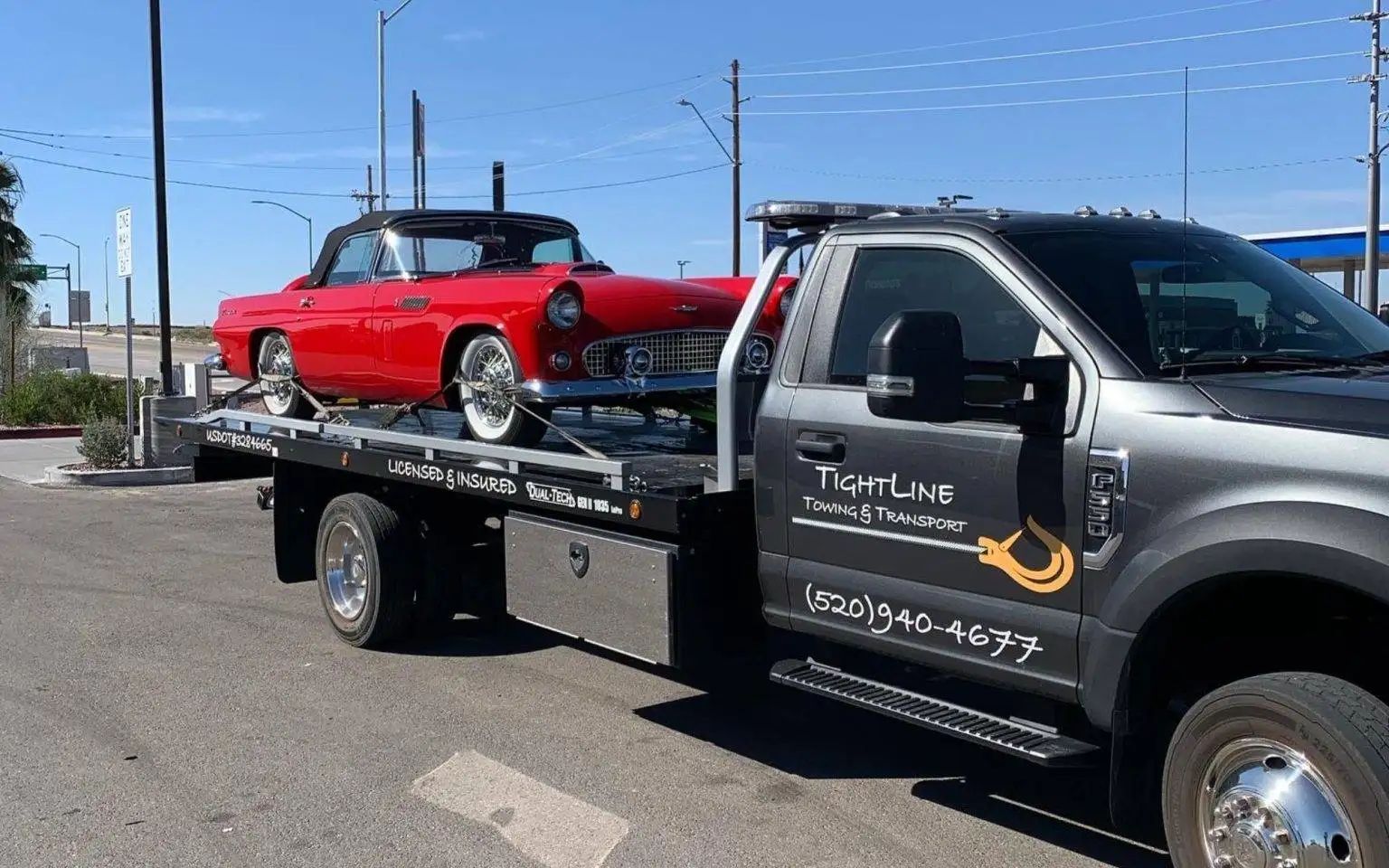 Red classic convertible car being towed by a tow truck on a sunny day.
