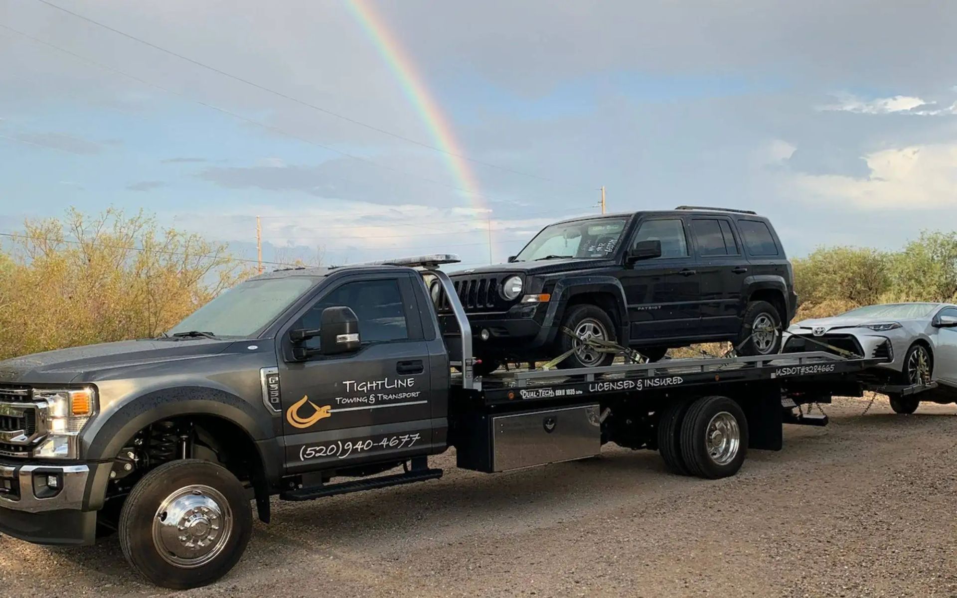 Tow truck hauling two cars under a rainbow.