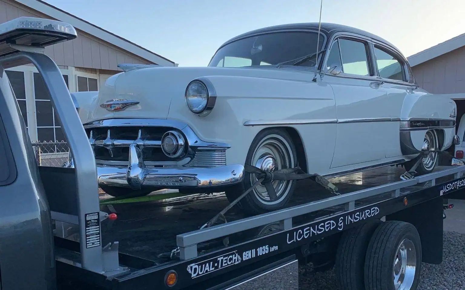 White and black vintage Chevrolet being towed on a flatbed tow truck.