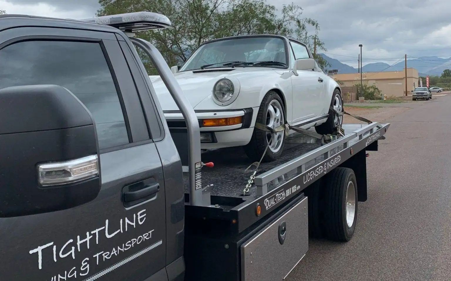 White vintage Porsche on a flatbed tow truck, being transported on a road.