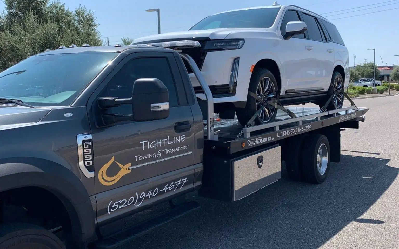 Tow truck carrying a white SUV on a sunny day. The truck has 