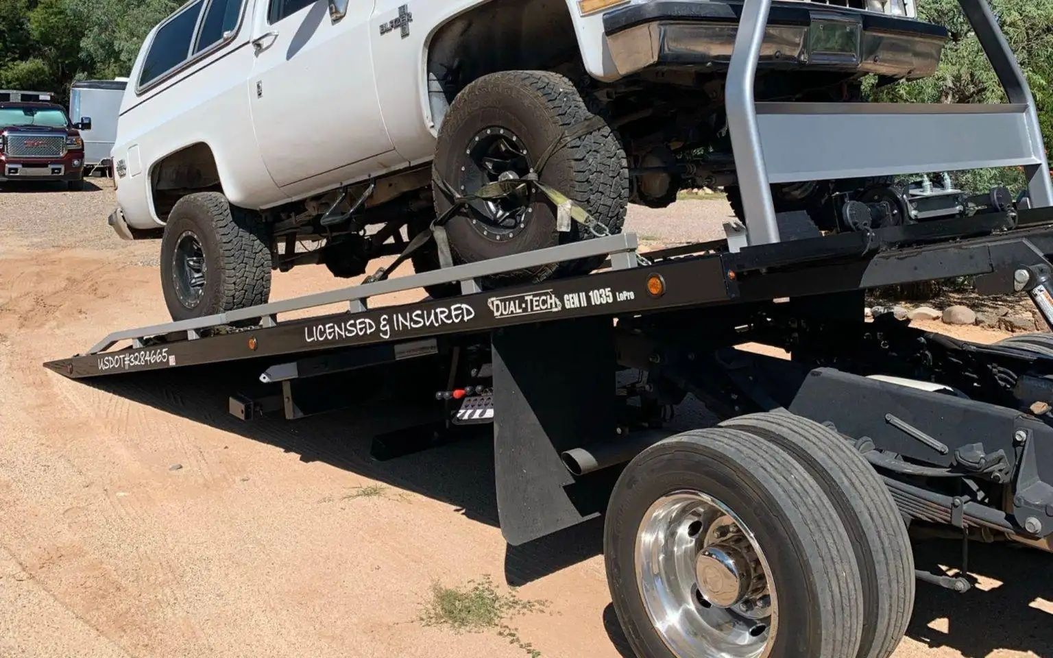 White SUV being loaded onto a flatbed tow truck on a dirt road.
