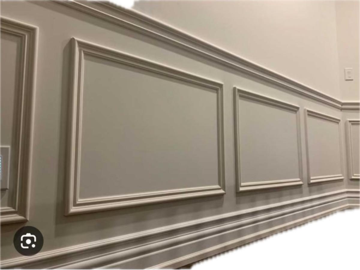 A wall with beige wainscoting featuring rectangular panel molding and decorative trim.