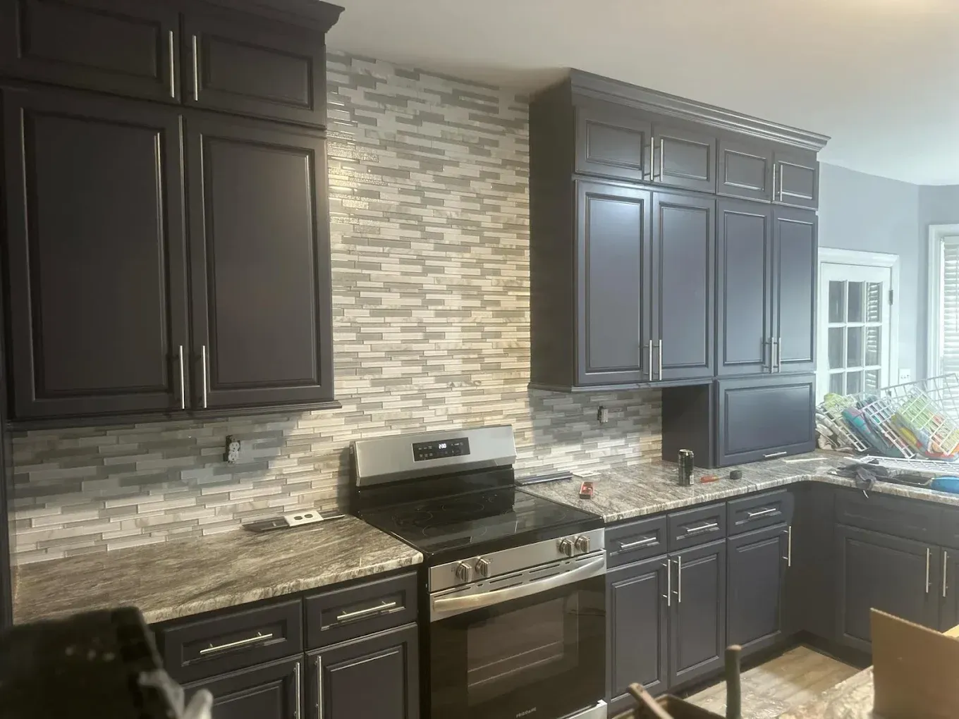 Dark blue kitchen cabinets with a grey stone backsplash and grey countertops.