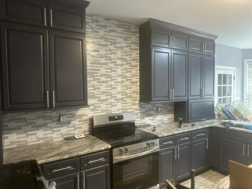 A kitchen with black cabinets , granite counter tops , and a stove.