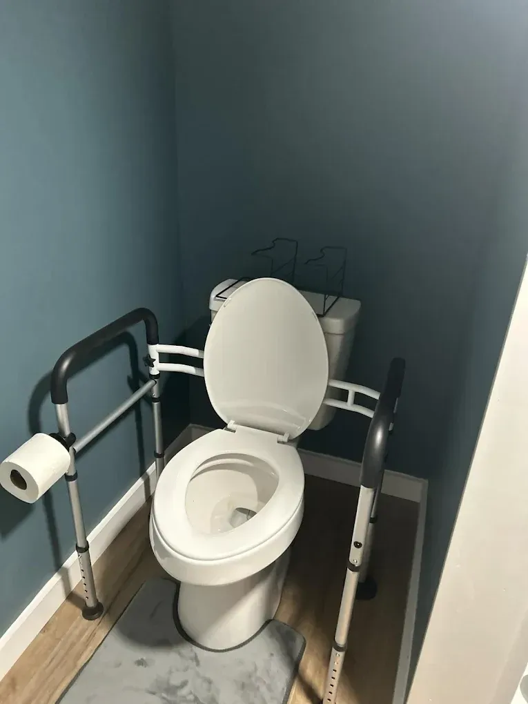 Toilet with raised seat, safety rails, and toilet paper roll in a blue-walled bathroom.