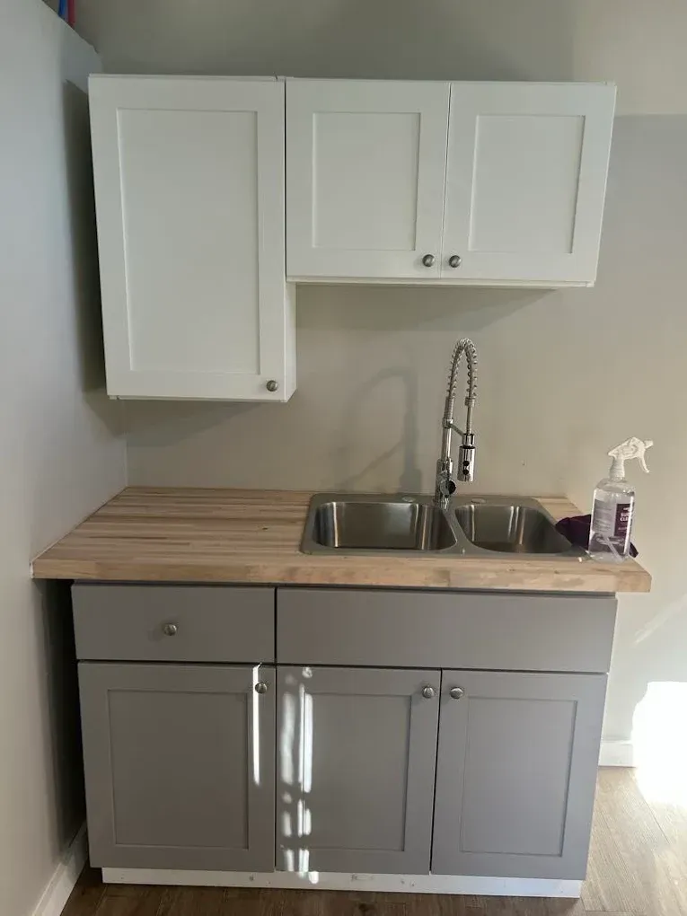 Gray and white utility sink cabinet with overhead white cabinets and wooden countertop.