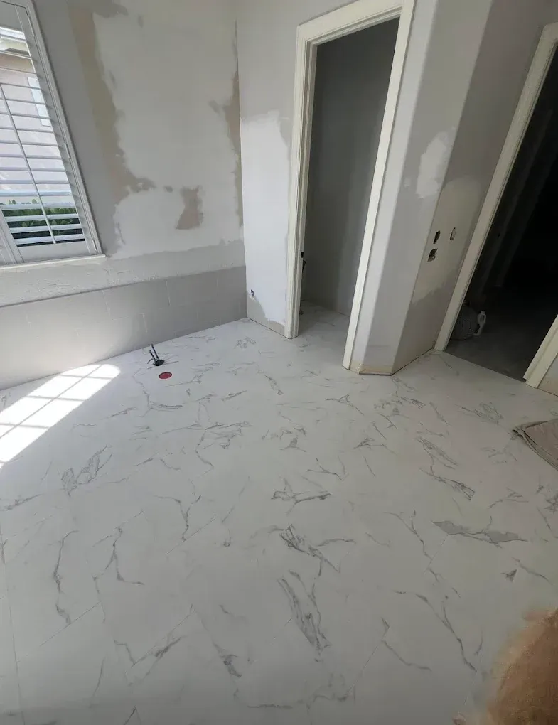 Room with marble-look tile floor, unfinished walls, two doorways, and a window with blinds.