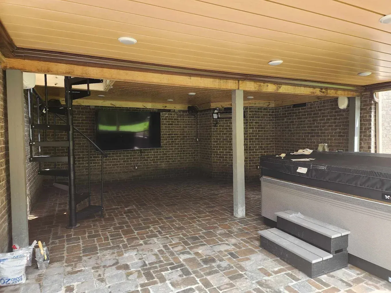 Brick patio with a spiral staircase, hot tub, and TV under a wood-paneled ceiling.