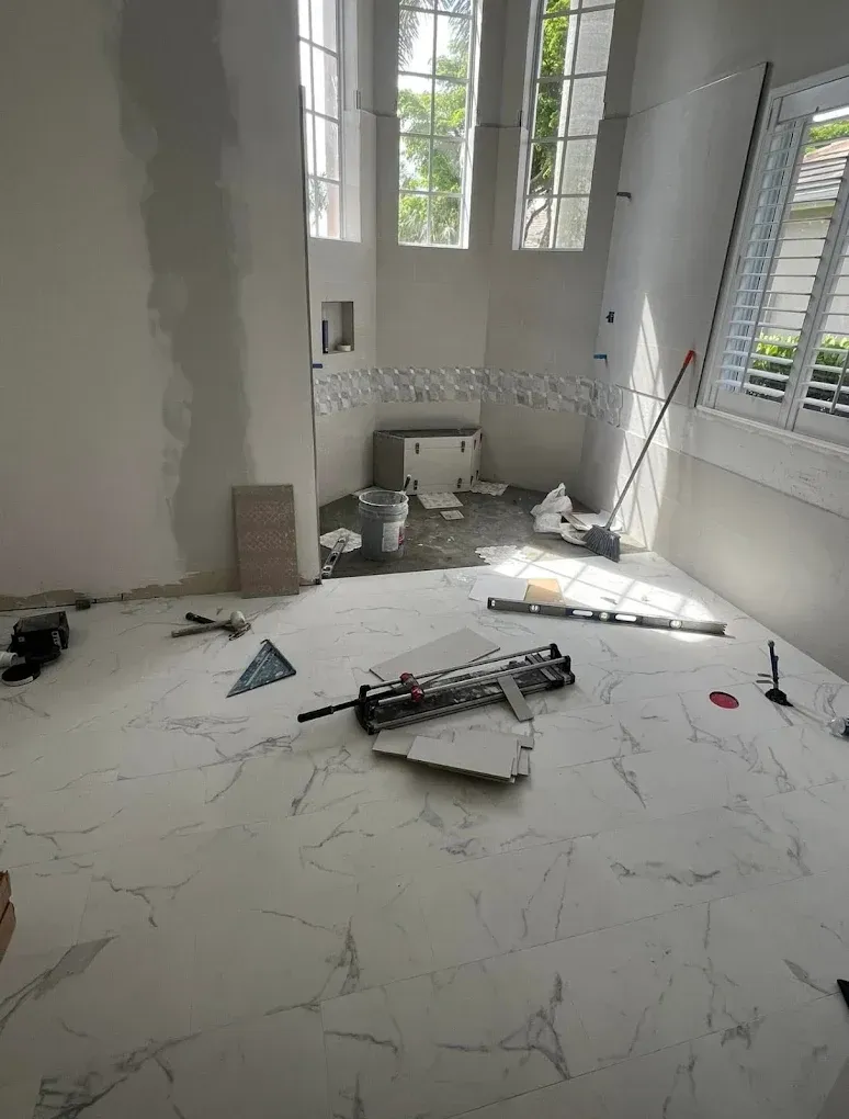 Bathroom under construction with large, white marble-look tiles, tools, and unfinished walls.