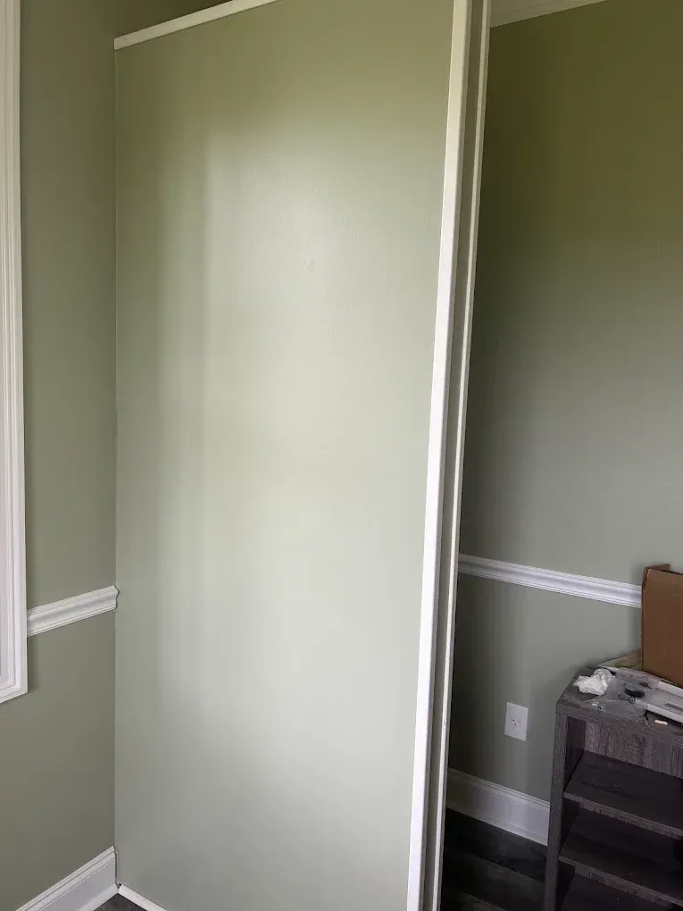Two green walls and white trim in a room, with a cabinet in the corner.