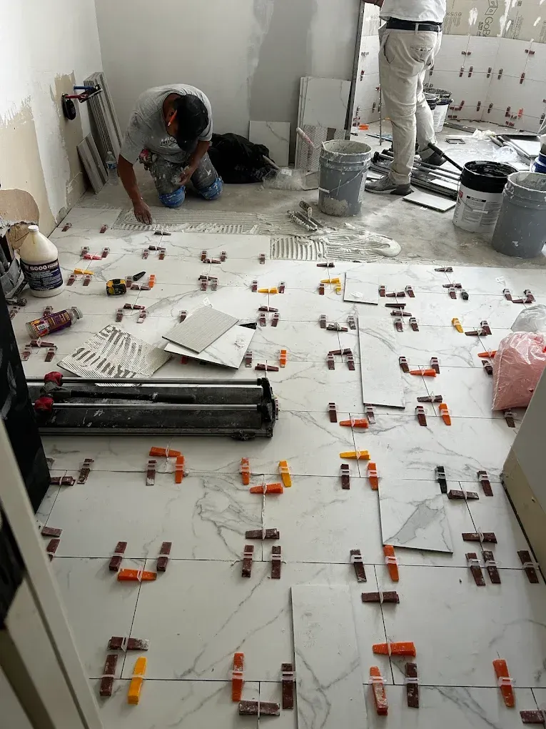 Two workers tiling a room; tiles are laid with leveling clips and spacers.