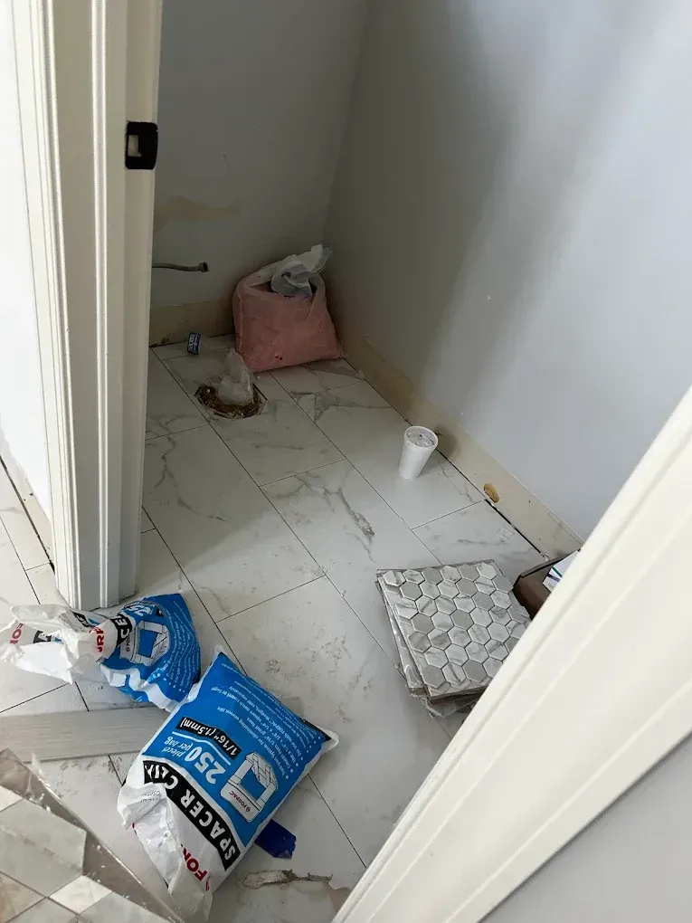 A cluttered small storage closet with tile floor, bags, and debris. Doorway on the left.