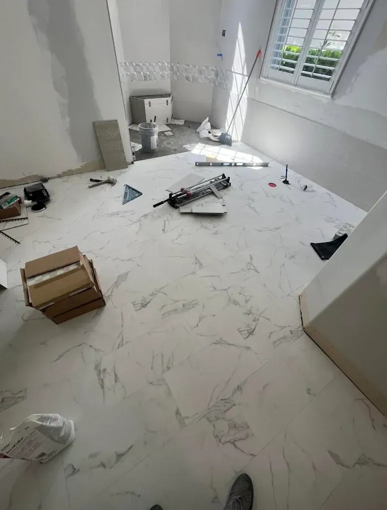 Bathroom under construction with marble-look flooring, tools, and open boxes.