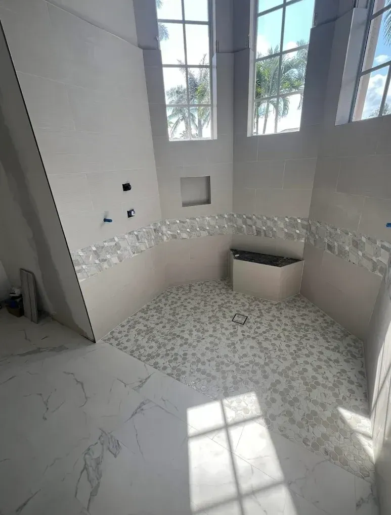 Bathroom under construction with mosaic tiles and white walls, featuring natural light from windows.
