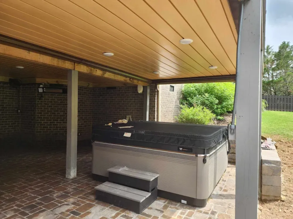 A hot tub is sitting under a covered patio.