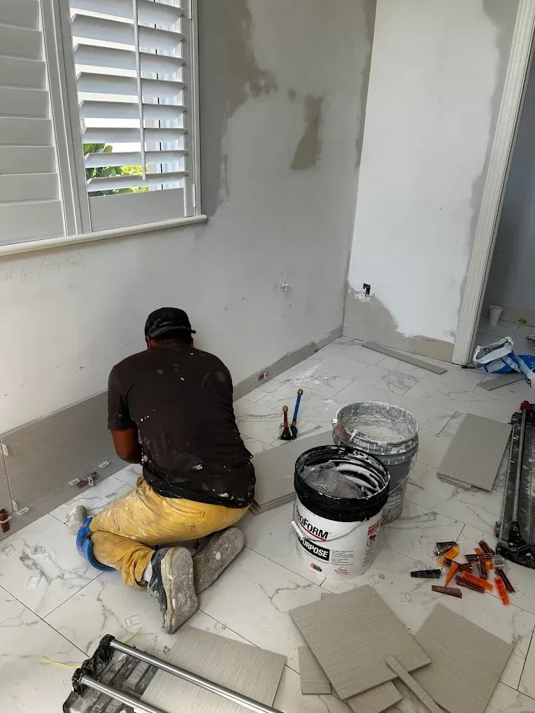 A man is kneeling on the floor in a room painting a wall.
