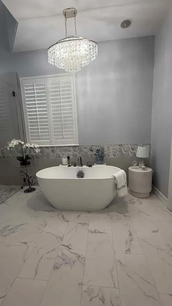 Elegant bathroom with white soaking tub, chandelier, and marble floors.