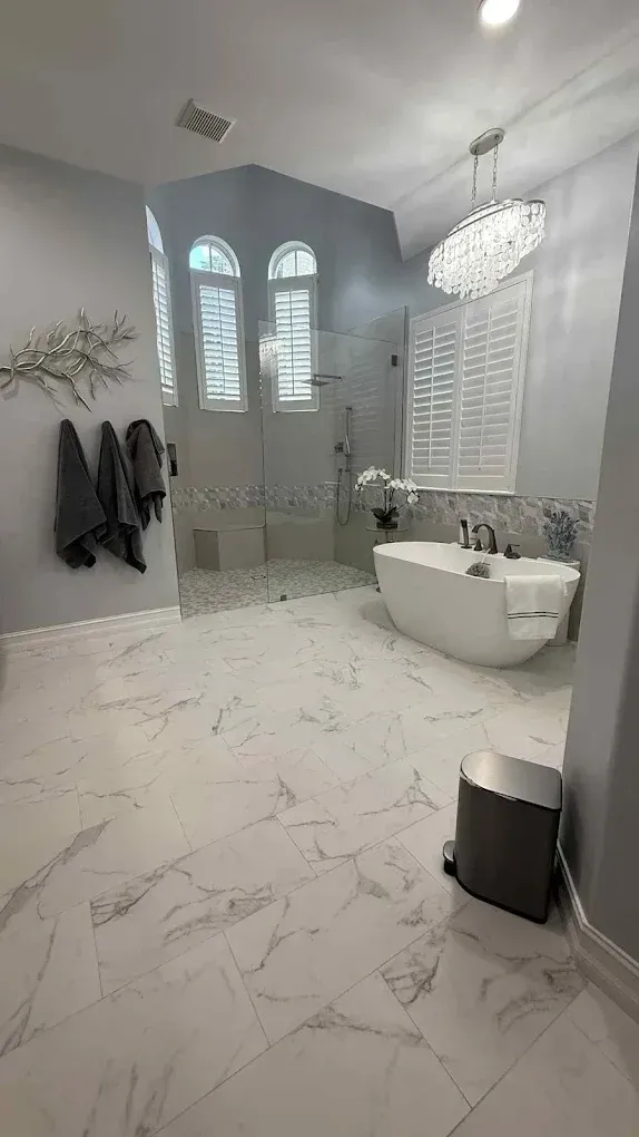 Spacious bathroom with marble floors, a white tub, and walk-in shower, and a large window.