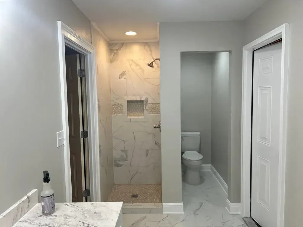 Bathroom with shower, toilet, and vanity. Gray walls, white trim, marble-like tile.