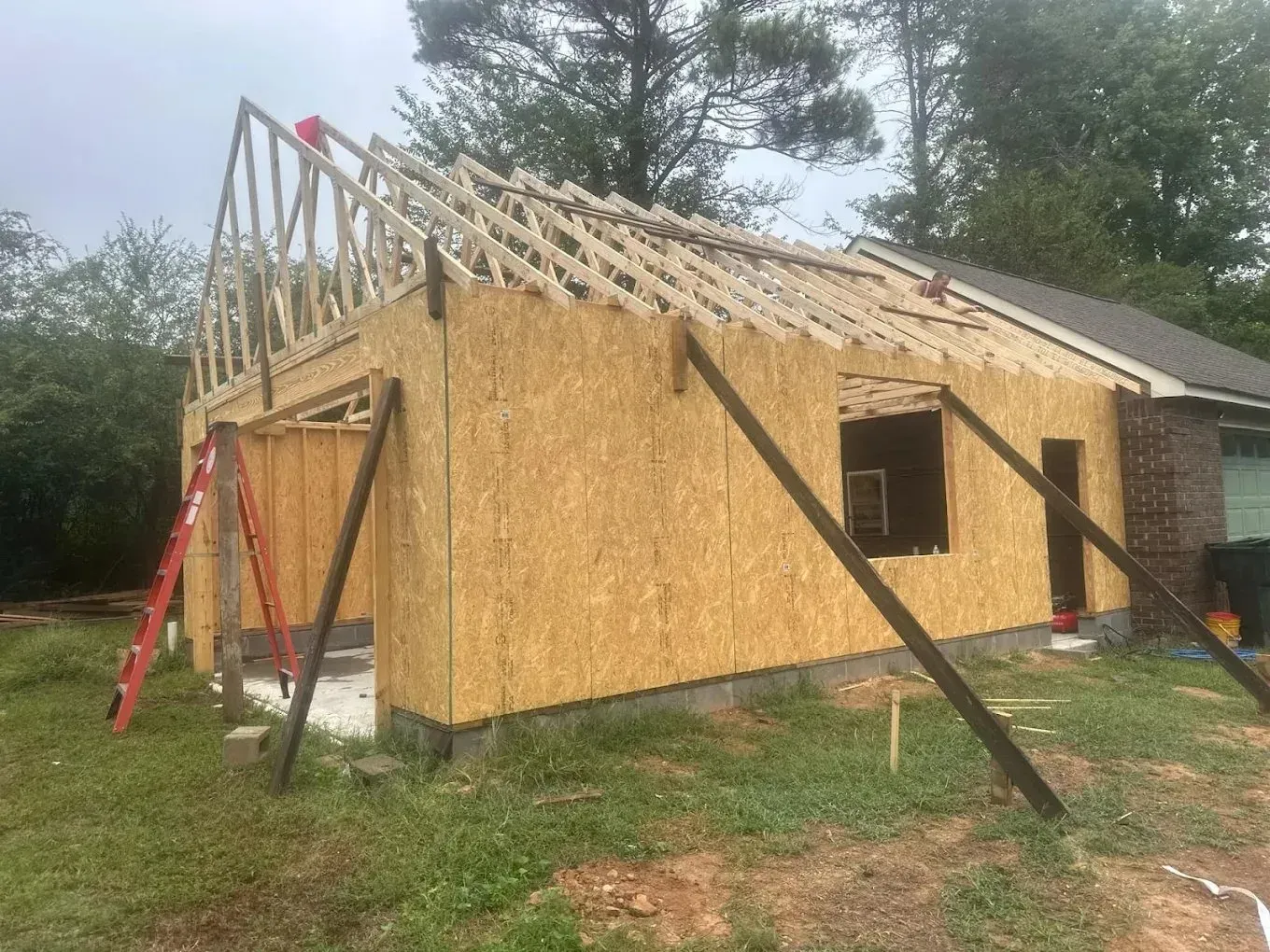 Garage under construction; OSB walls, roof trusses, with supporting beams, and ladder.