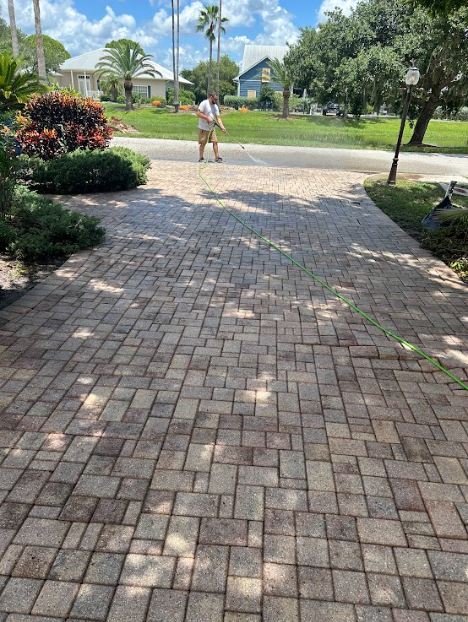 Brick driveway with a person standing at the end, houses and trees in the background on a sunny day.