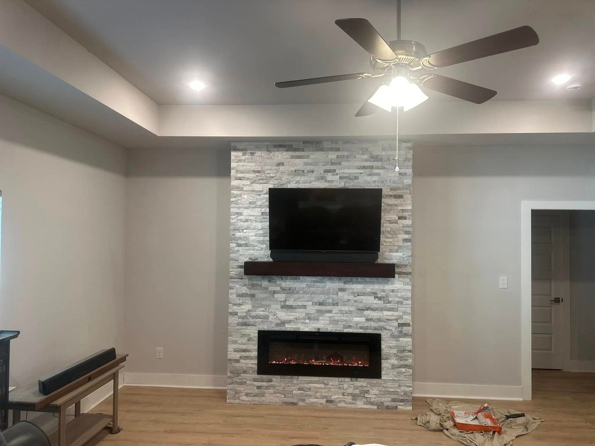 Living room with fireplace, TV, and ceiling fan against a stone accent wall.