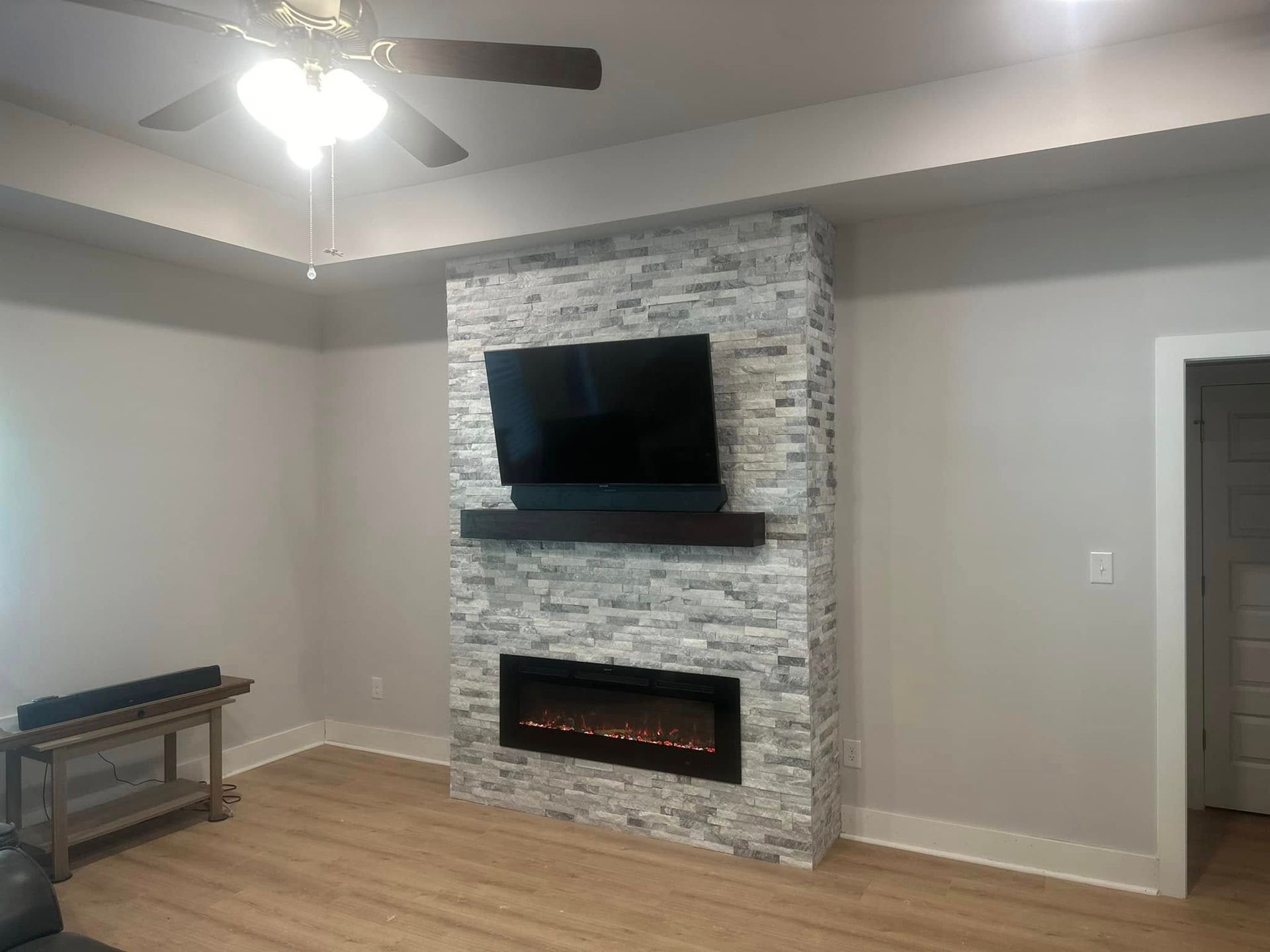 Living room with fireplace, TV, and wooden mantel against a stone accent wall.
