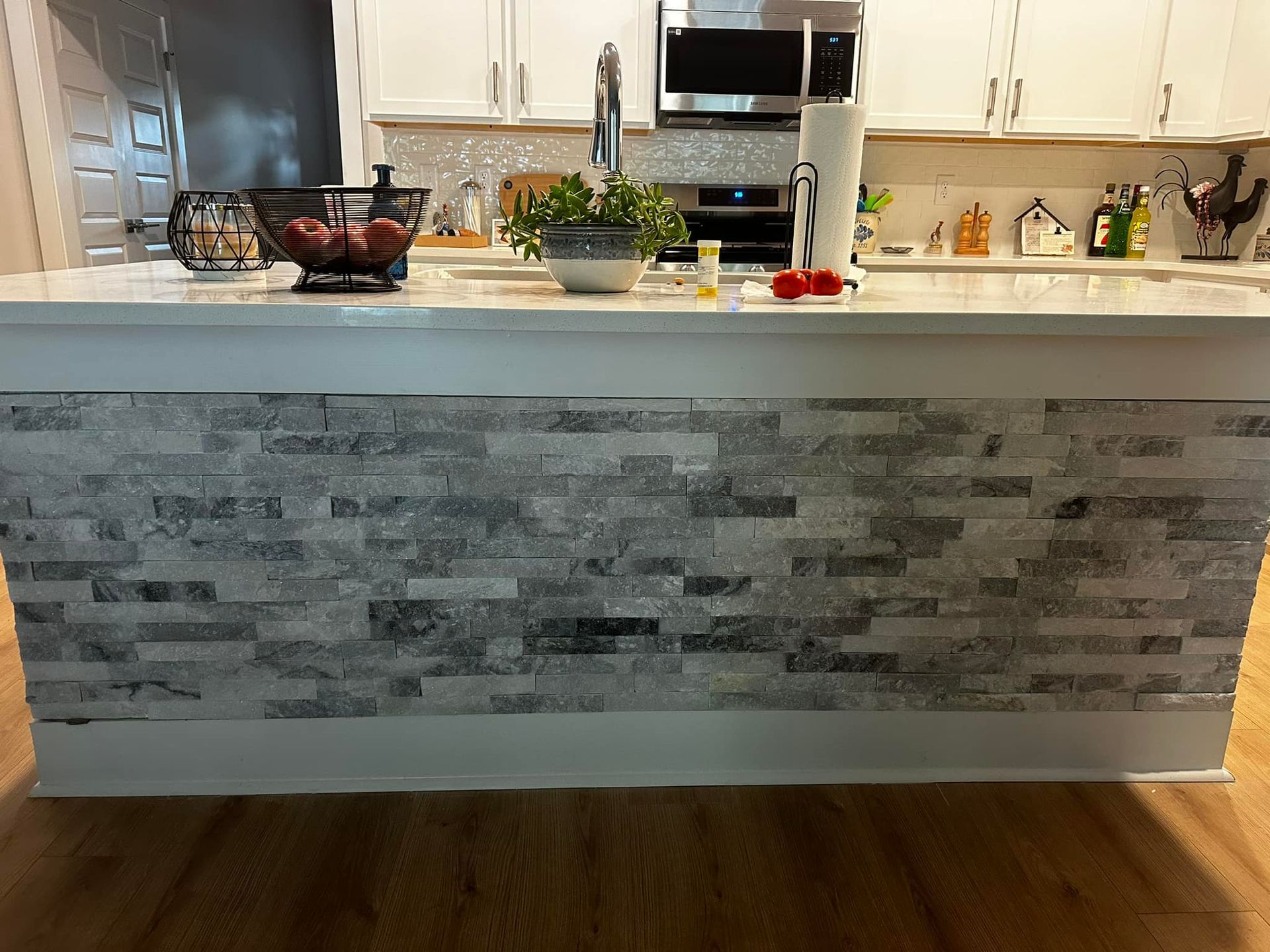 Kitchen island with stone facing, white cabinets, and wooden floor.