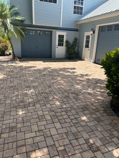 Paver driveway in front of a light blue house with garage doors and a white door.