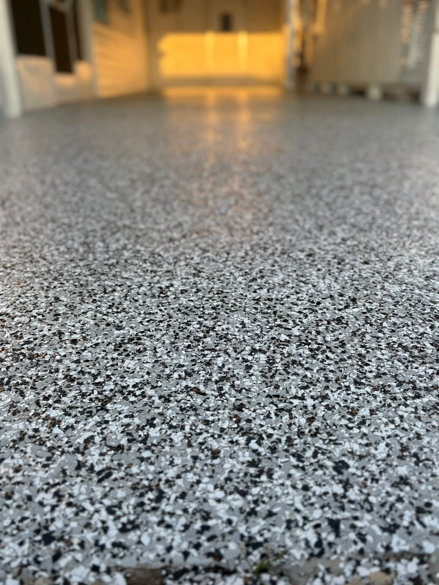 Close-up of a garage floor with a decorative epoxy finish featuring a speckled black, white, and gray chip pattern.