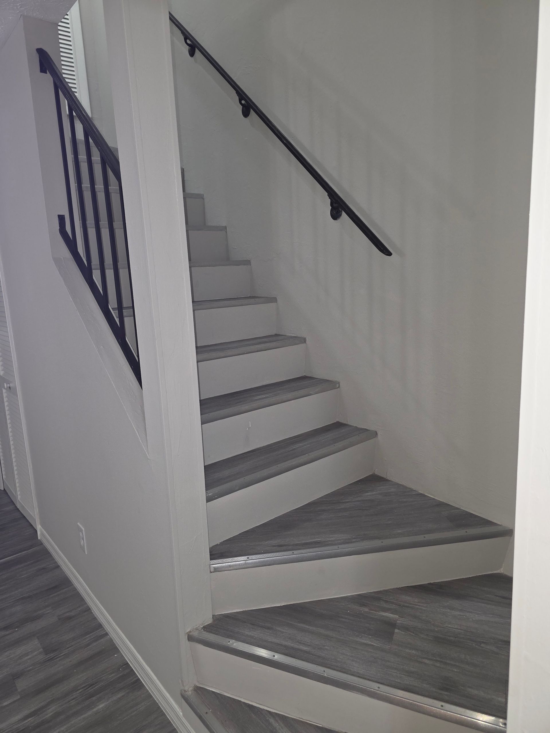 Man tiling a wall, kneeling on tile floor in a room with window, buckets of supplies nearby.