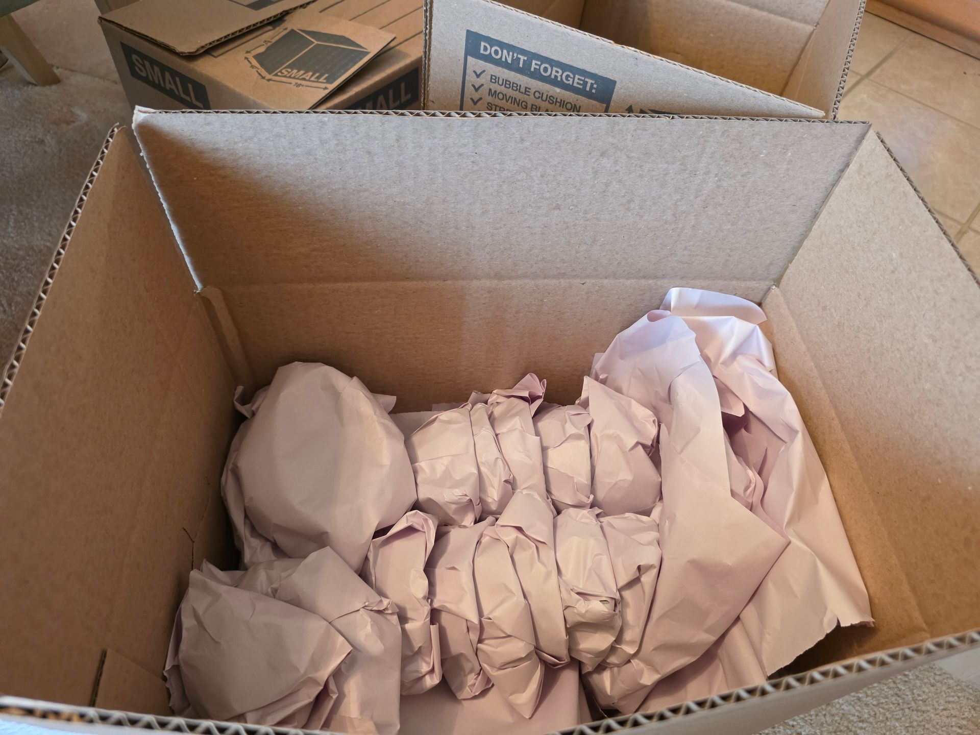 A cardboard box packed with items individually wrapped in light-colored protective paper.