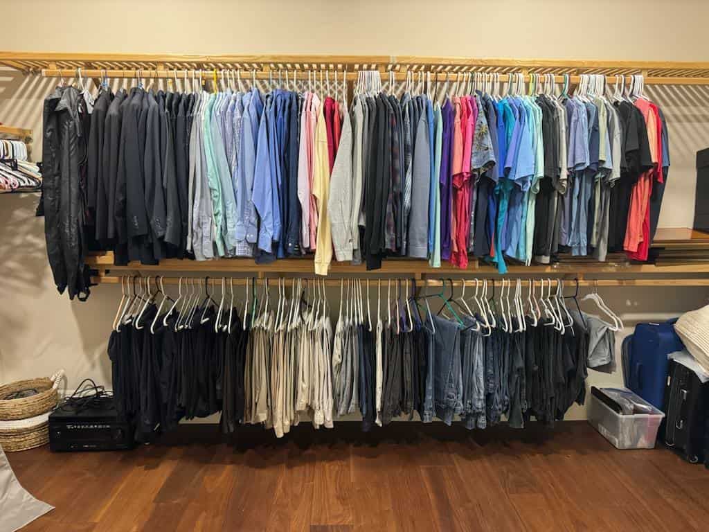 A closet with two rows of clothing hanging on wooden rods, featuring a mix of shirts and pants in various colors.