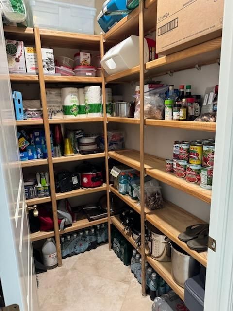 A walk-in pantry with wooden shelves filled with kitchen supplies, canned goods, paper towels, and water bottles.