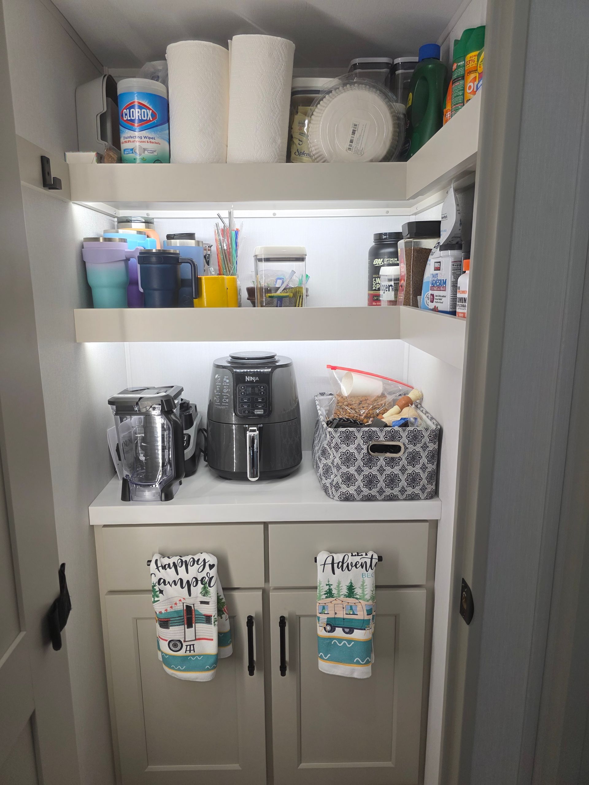 A well-lit, organized kitchen pantry with two shelves holding dry goods above a counter with appliances and base cabinets.