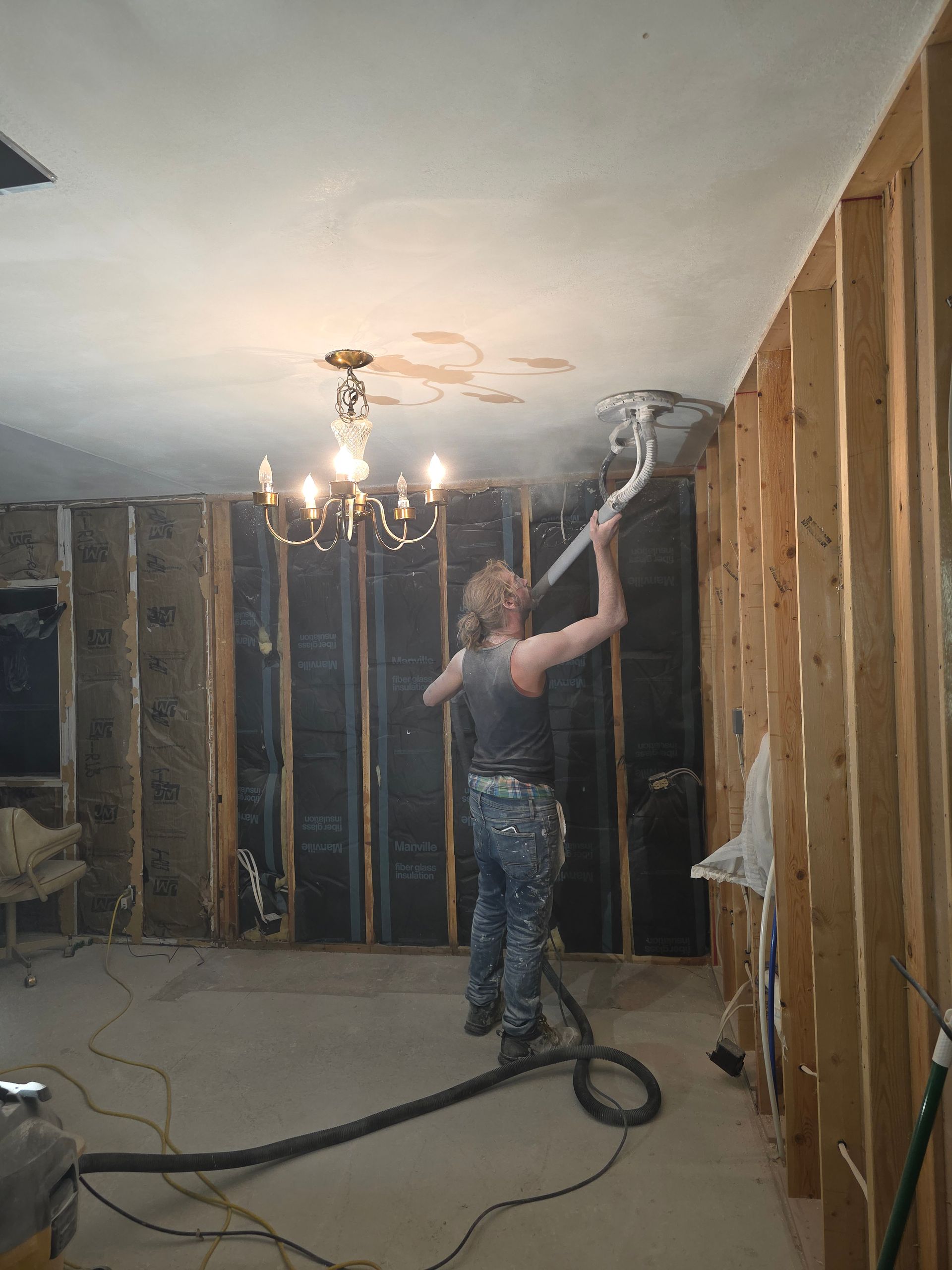 A person in a room under construction uses a long hose to spray insulation into the wall cavity.