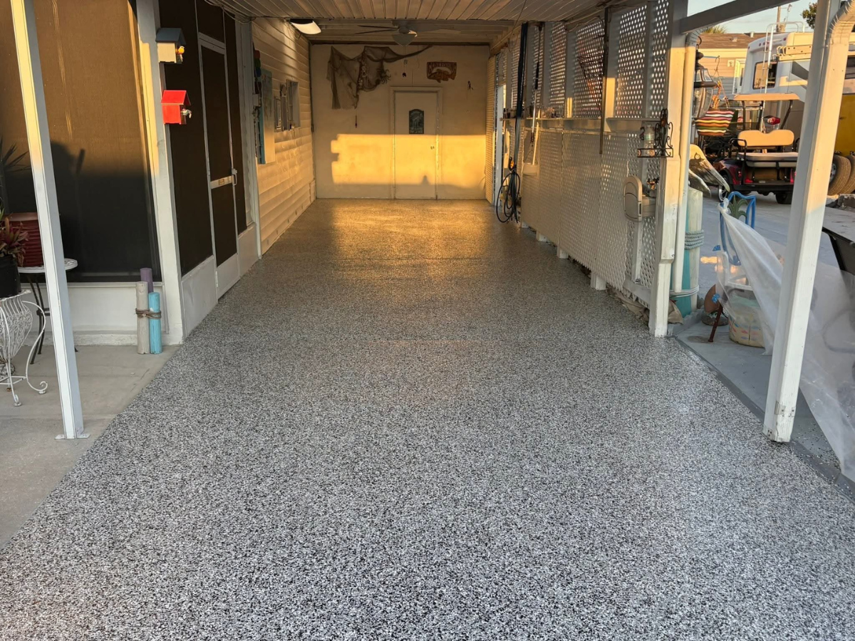 A covered patio or carport with a glossy, light-colored speckled epoxy floor in an outdoor residential setting.
