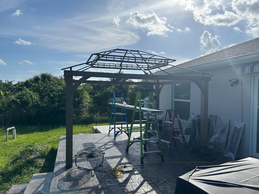 Gazebo under construction on a patio, set against a blue sky and green yard.