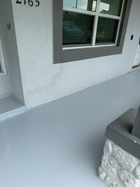 Gray painted porch with white stucco wall. Window with gray trim.