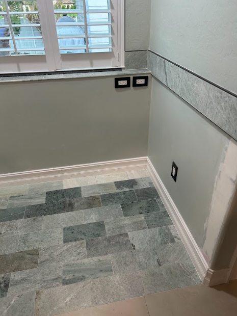 Bathroom corner with green stone floor, light green walls, decorative tile border, and window with shutters.