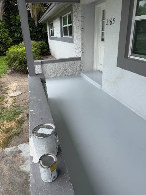 A newly painted porch with gray paint. Two paint cans sit on the railing. House number 