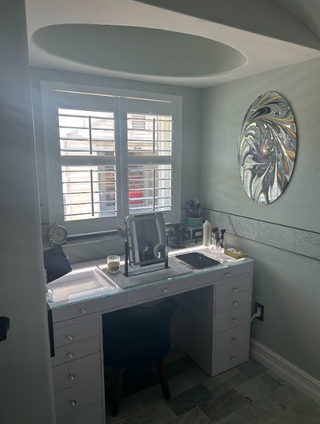 Makeup vanity in a mint-colored room, with a window, mirror, and decorative wall mirror.