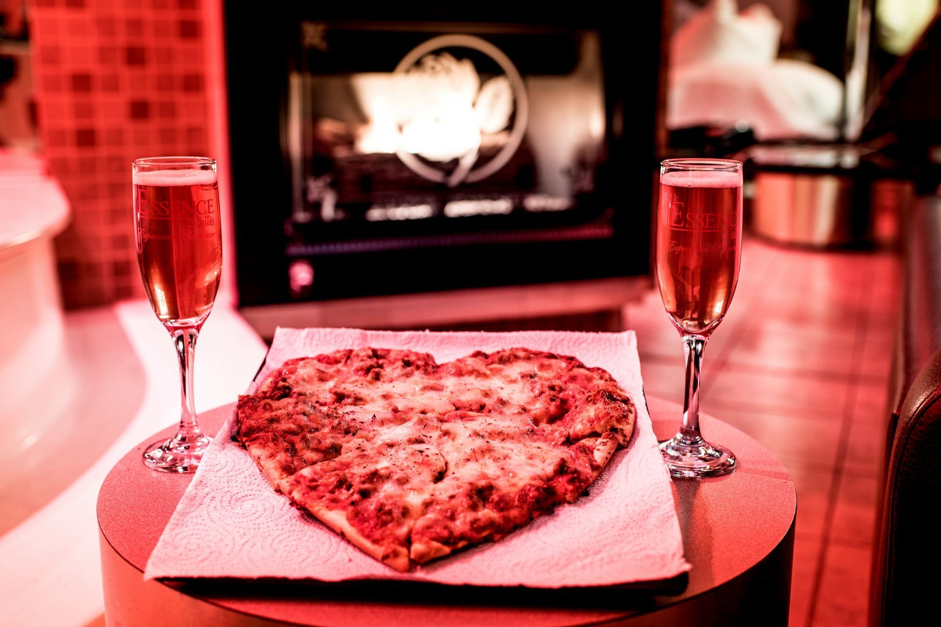 Heart-shaped pizza, two champagne flutes, and an oven in a warmly lit setting.