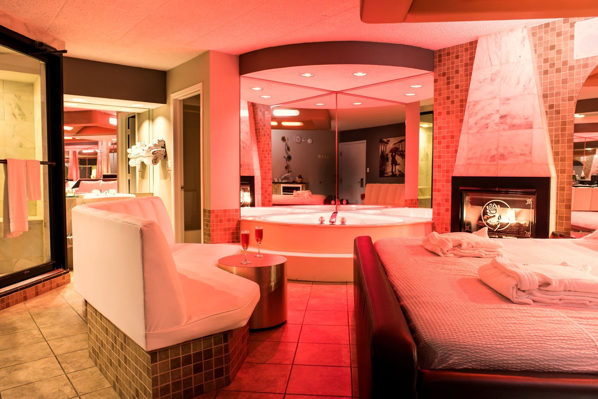 Romantic hotel suite with a fireplace, bed, jacuzzi, and red mood lighting.