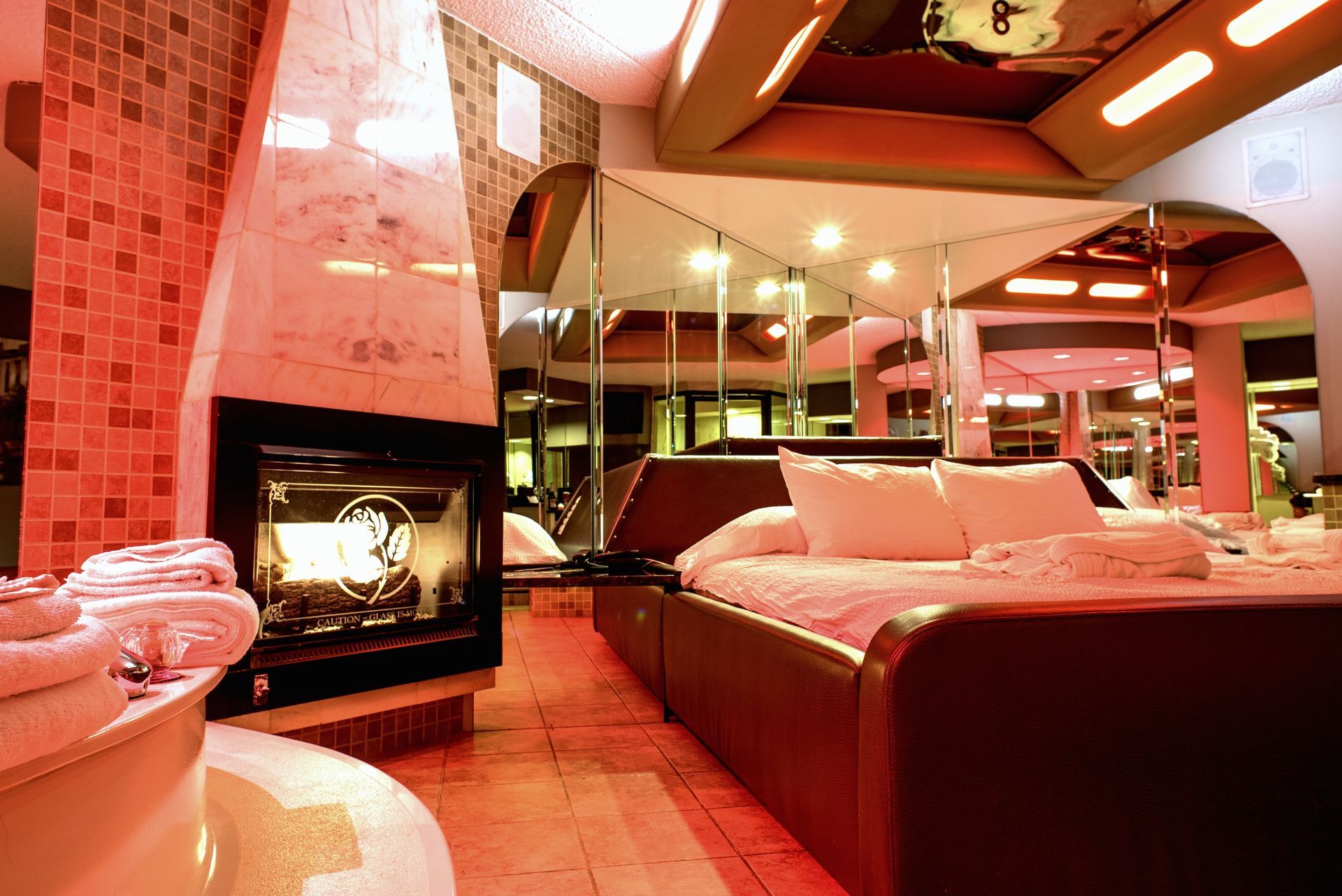 Romantic hotel room with a fireplace, jacuzzi, and mirrored ceiling, lit with red light.