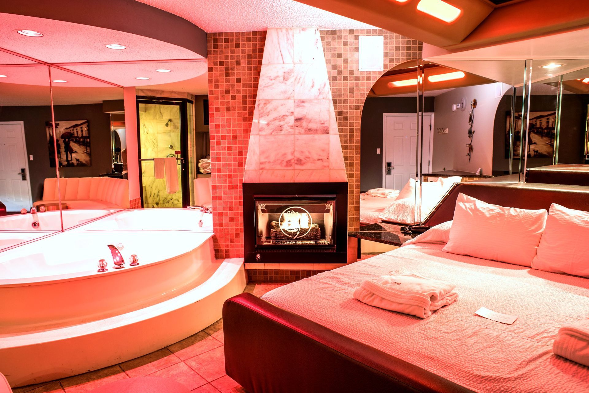 A romantic hotel suite with a jacuzzi, fireplace, and bed, all lit with red light.
